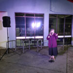 A woman stands outside Pt Chev library telling jokes into a microphone
