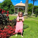 Tessa stands in front of a flower bed in the Auckland Domain. Behind that is the band rotunda.